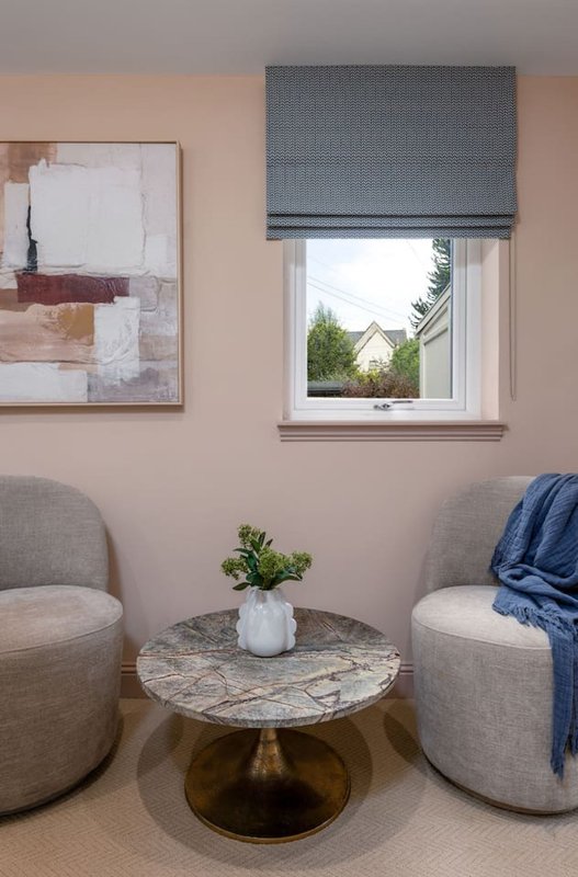 Modern sitting area with two grey upholstered chairs, small round table, abstract wall art and window