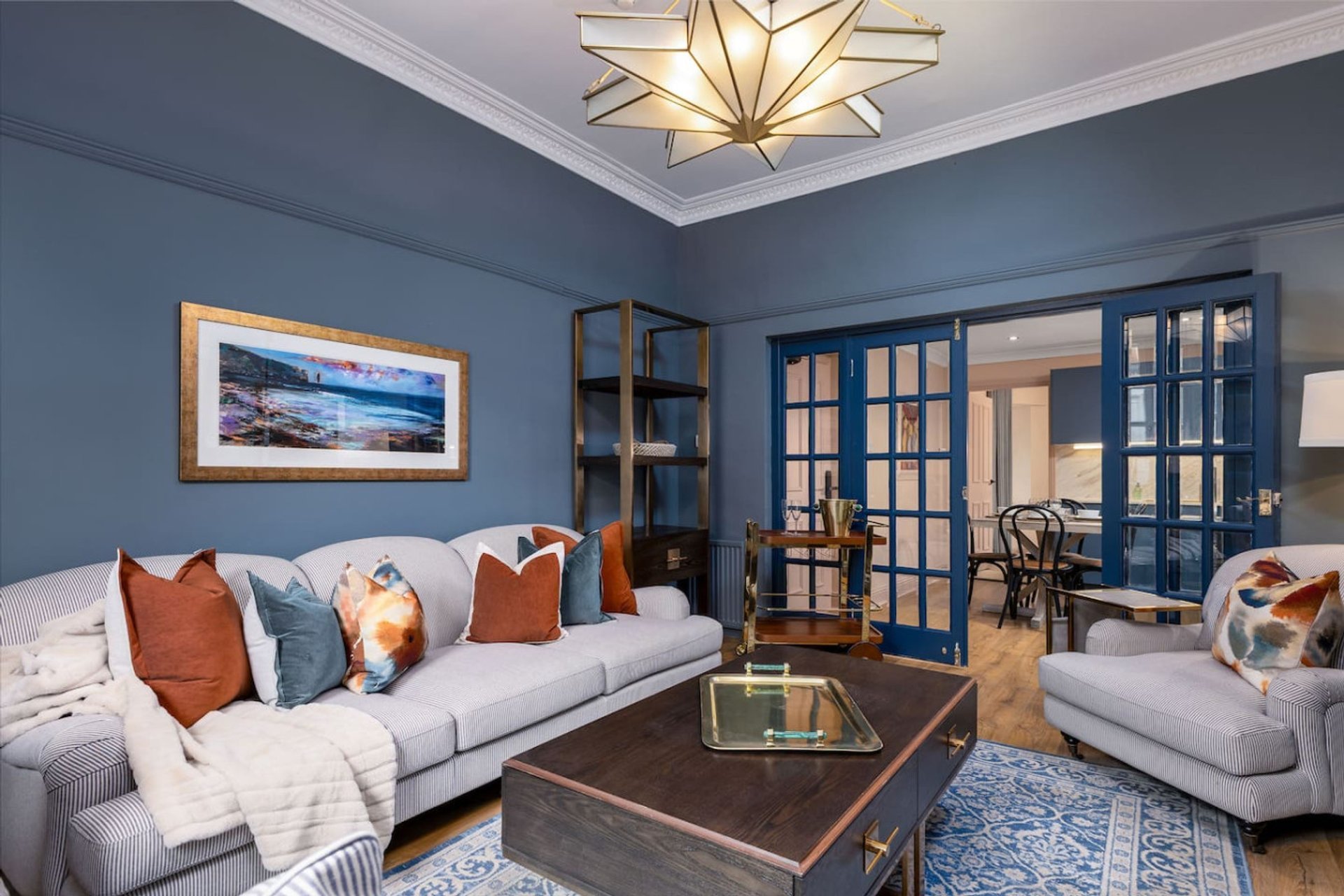 Modern living room with blue walls, white sofas, decorative pillows, framed artwork and geometric ceiling light