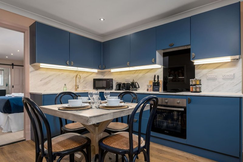 Modern kitchen and dining area with blue cabinetry, marble backsplash, and dining table with four chairs