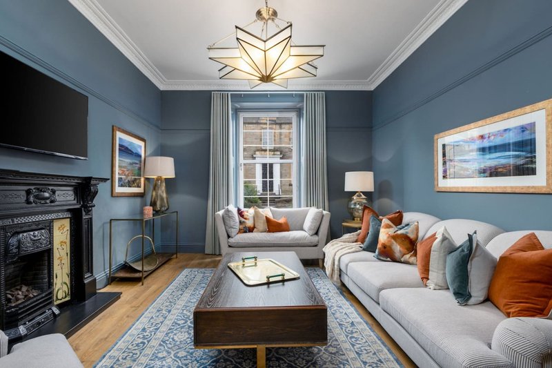 Blue sitting room with fireplace, cream sofa, window seat and framed artwork