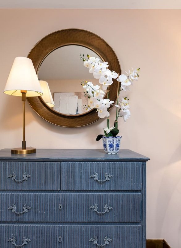 Bedroom dresser with round mirror, table lamp, and white orchid flowers in vase