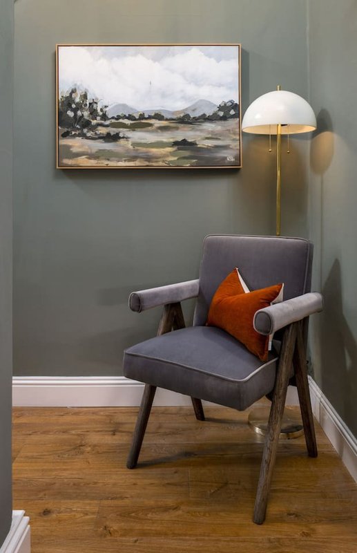 Modern armchair with orange cushion, brass floor lamp, and landscape artwork on grey wall