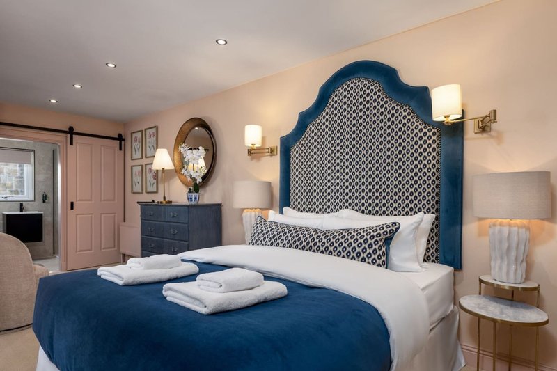 Bedroom with blue upholstered headboard, white bedding, blue throw, and bedside lamps