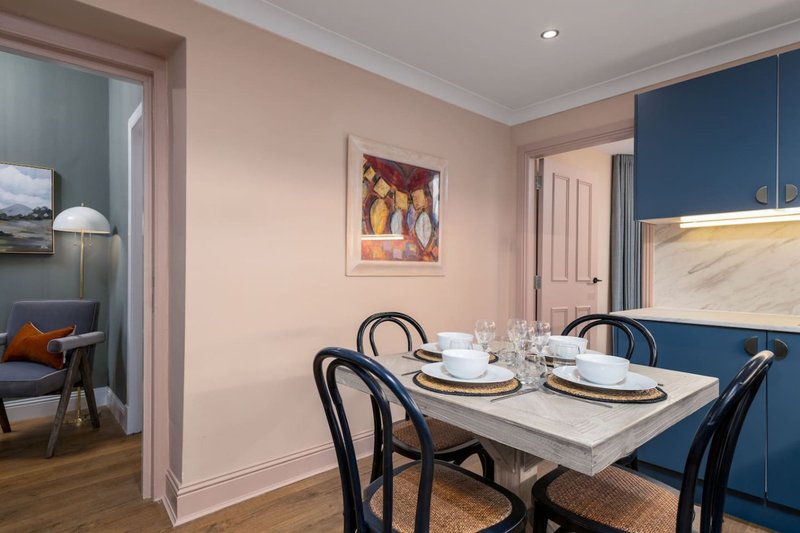 Modern dining room with white table, black chairs, and blue kitchen cabinetry visible