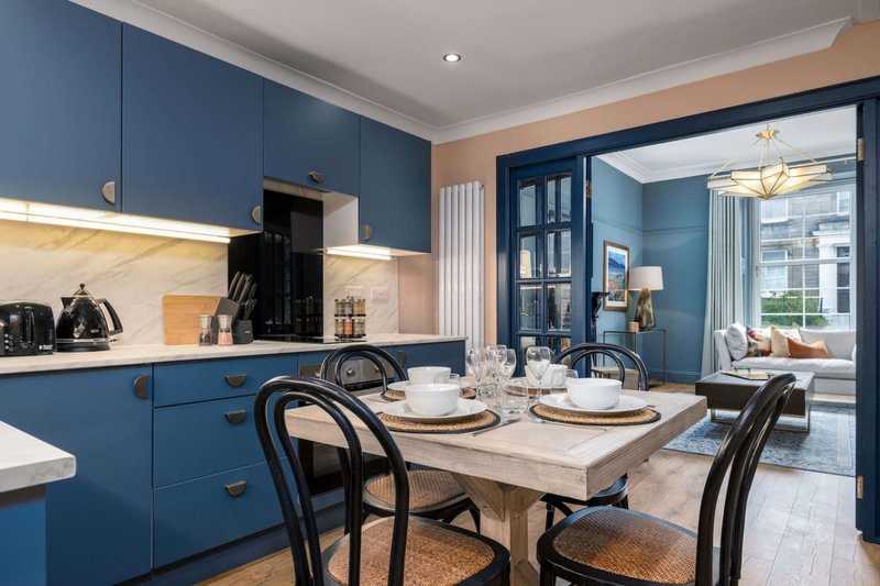 Modern kitchen-diner with blue cabinetry, dining table, chairs and open-plan living area
