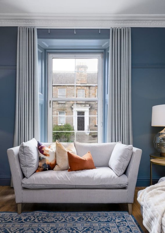 Modern living room with grey sofa, window seat, blue accent wall and striped curtains