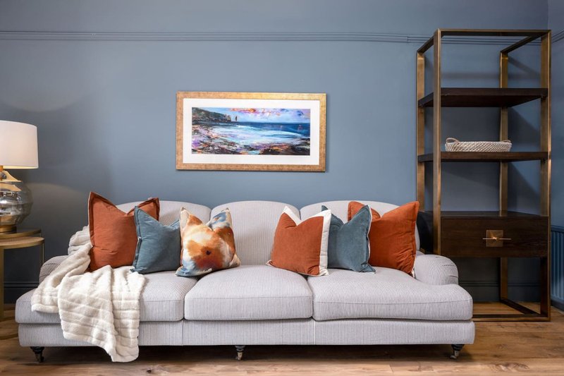 Modern living room with light grey sofa, decorative pillows, framed landscape art, and wooden shelving unit