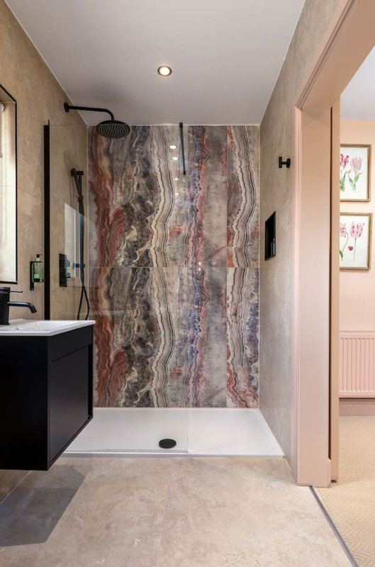 Modern bathroom with walk-in shower, black vanity, and neutral stone flooring
