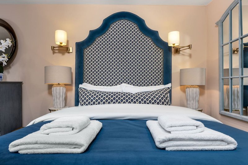 Bedroom with blue upholstered headboard, white bedding, matching bedside lamps and wall sconces