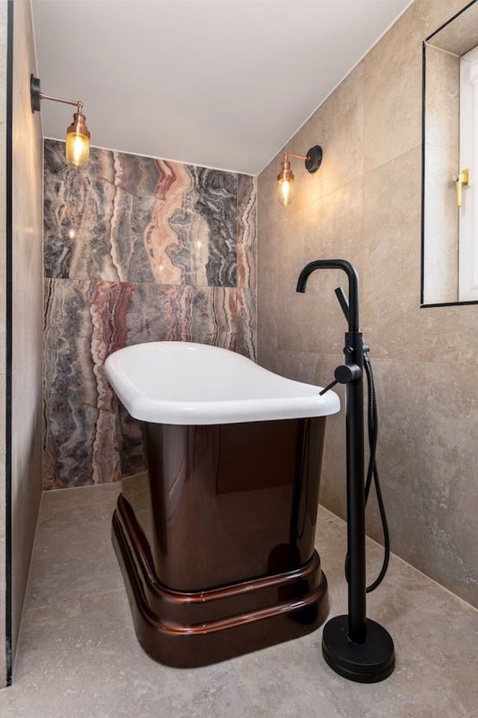 Modern bathroom with freestanding dark tub, marble feature wall, pendant lights and floor filler
