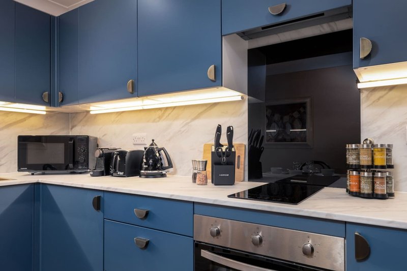 Modern kitchen with blue cabinetry, white countertop, stainless steel appliances and under-cabinet lighting