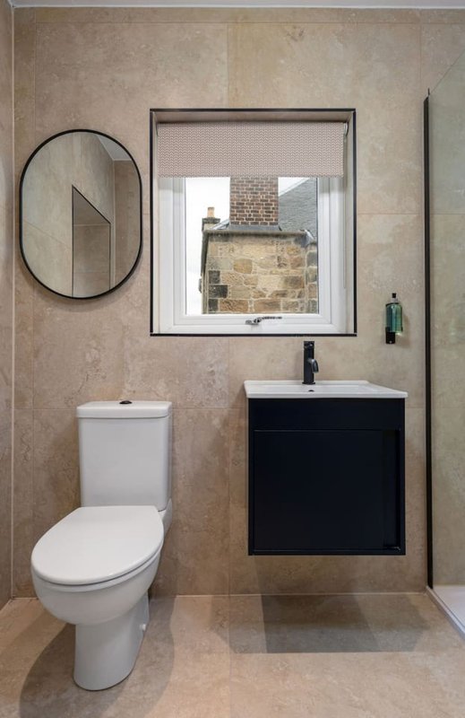 Modern bathroom with toilet, black vanity sink, round mirror and tiled walls