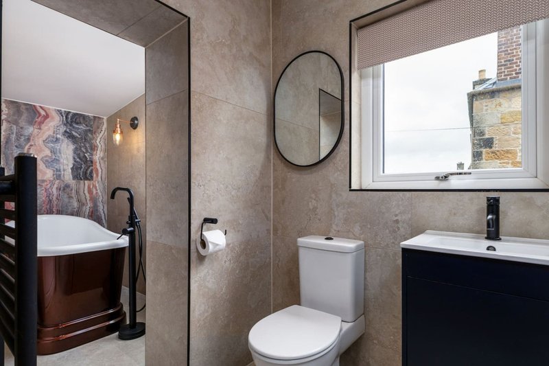 Modern bathroom with dual vanities, toilet, oval mirror and tiled walls