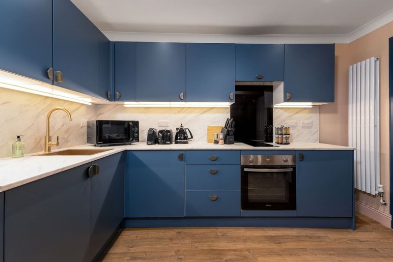 Modern kitchen with blue cabinetry, marble backsplash, built-in appliances and wooden flooring