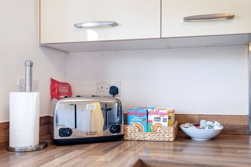 Kitchen counter with toaster, cereal boxes, paper towel holder and white cabinets above