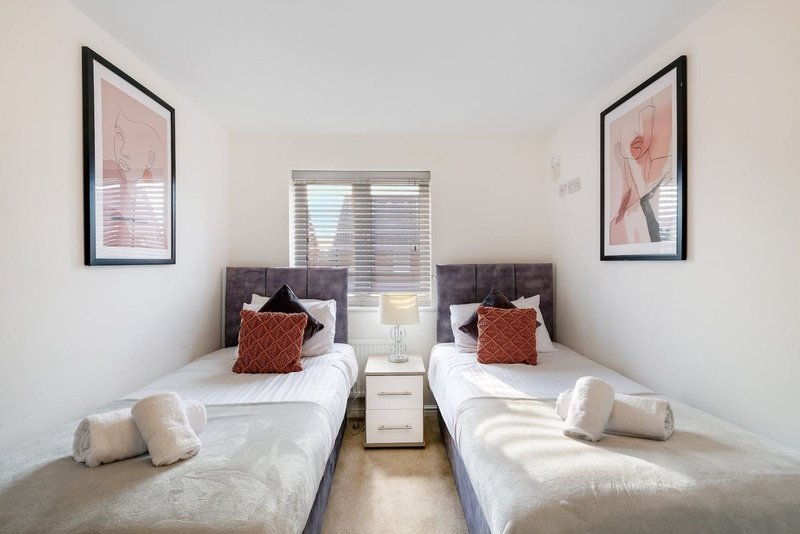 Twin bedroom with two single beds, white bedding, red cushions, framed wall art and central window
