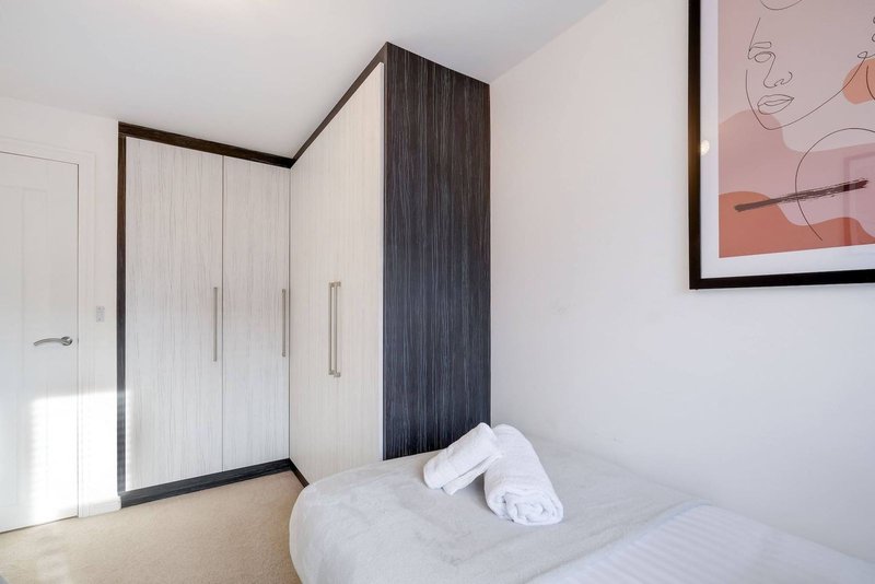 Modern bedroom with double bed, white bedding, dark wood wardrobe and framed wall art