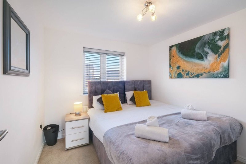 Bedroom with double bed, grey headboard, yellow cushions, bedside table and wall art