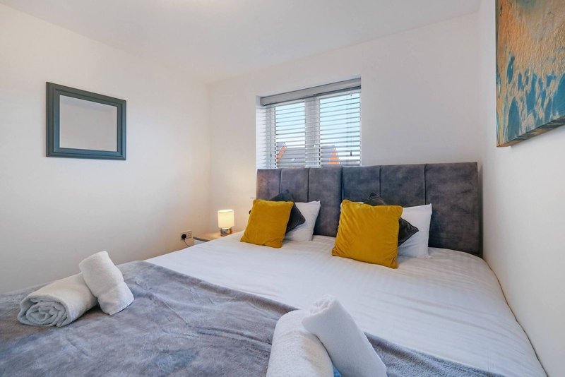 Modern bedroom with double bed, gray upholstered headboard, yellow and white pillows, and shuttered window