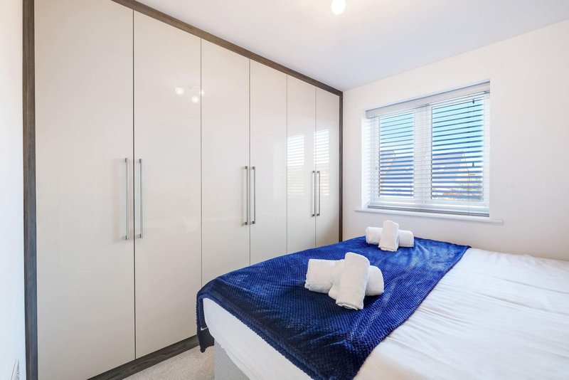 Modern bedroom with double bed, blue throw, white pillows, and fitted wardrobe