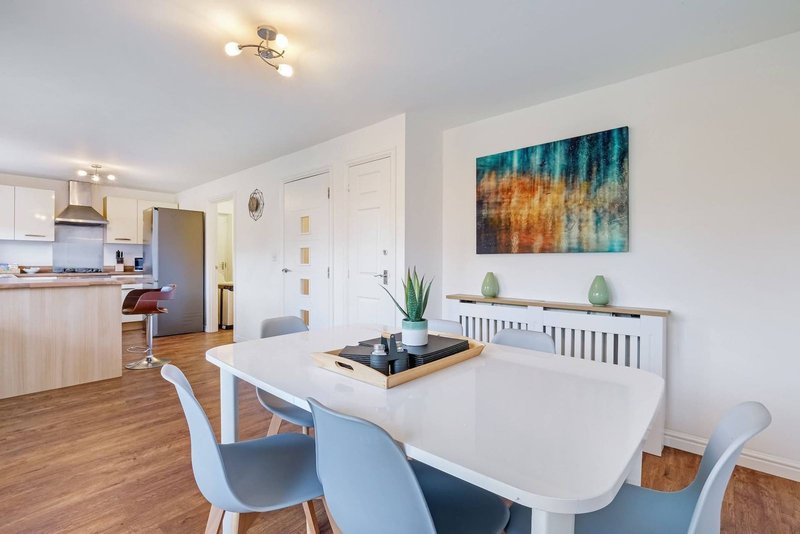Open-plan dining and kitchen area with white table, blue chairs, and woodland artwork