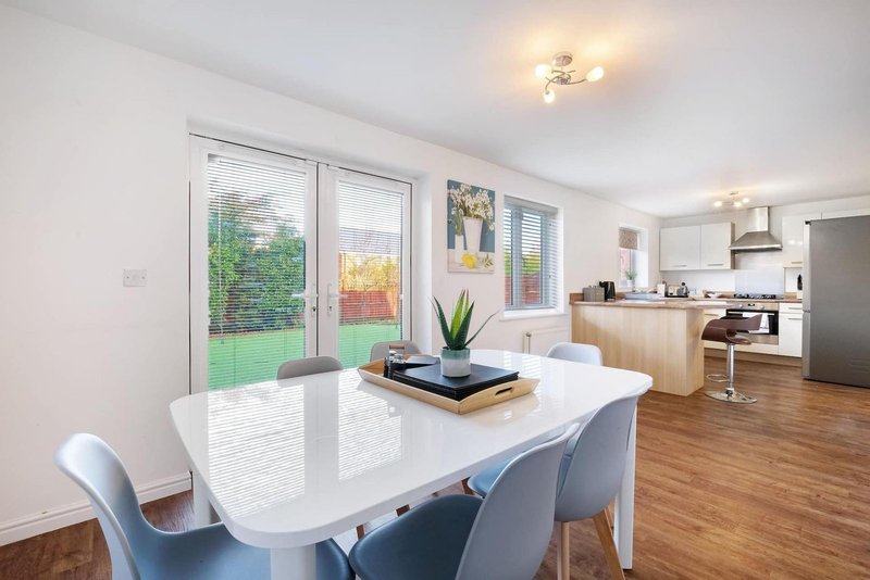 Open-plan dining and kitchen area with white table, blue chairs, wood flooring and garden views