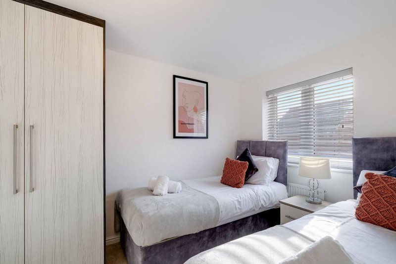 Bright bedroom with twin beds, wardrobe, framed artwork, and window with blinds
