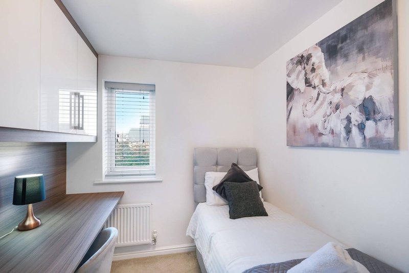 Compact bedroom with single bed, desk, kitchenette and window with city view