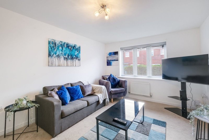 Living room with gray sofa, blue cushions, glass coffee table and wall-mounted TV