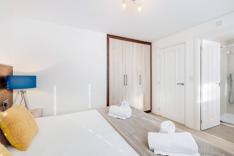 Bright modern bedroom with white bed, yellow cushion, wooden headboard, and built-in wardrobes