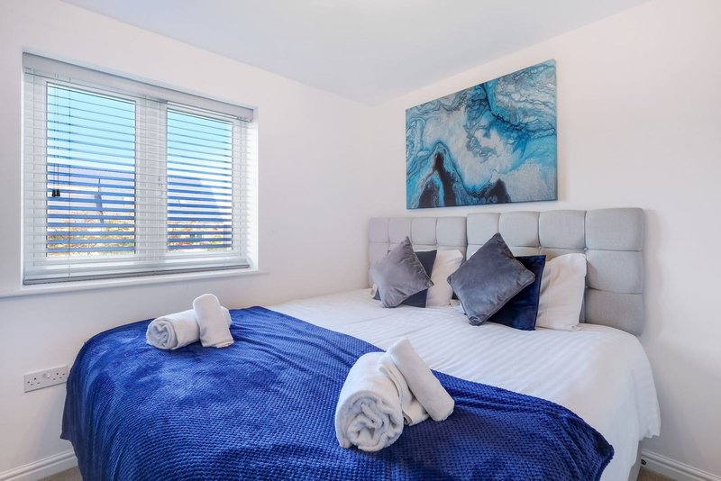 Modern bedroom with double bed, blue throw, white rolled towels and grey headboard
