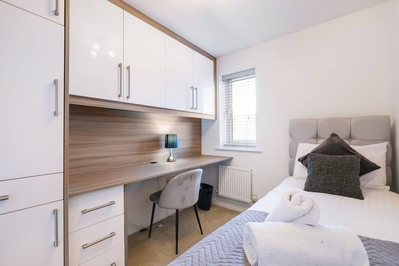 Bright bedroom with single bed, built-in desk, white cabinetry and wooden backsplash
