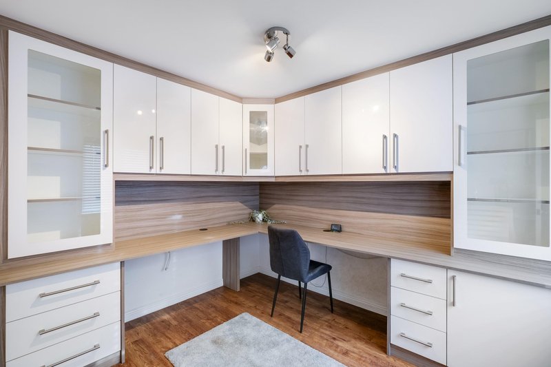 Home office with white cabinetry, wooden desk, office chair, and hardwood flooring