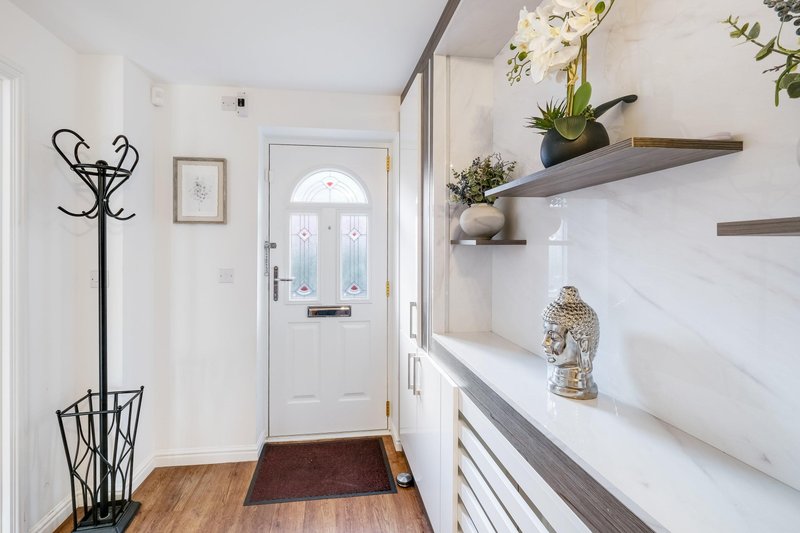 Bright hallway with wooden floor, white door, coat stand, shelves with plants and decorative items