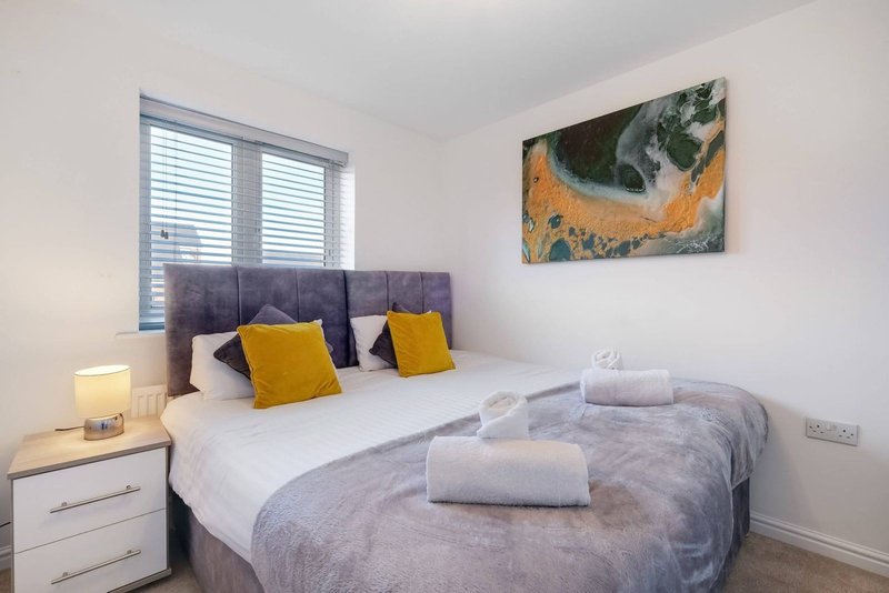 Modern bedroom with double bed, gray headboard, yellow cushions, and white bedside table