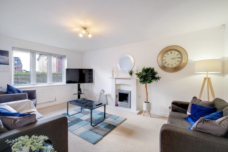 Bright living room with grey sofas, fireplace, wall-mounted TV and wooden clock