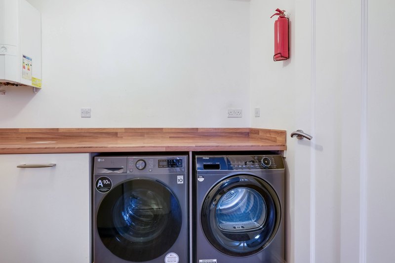 Utility room with side-by-side washing machine and tumble dryer under wooden counter