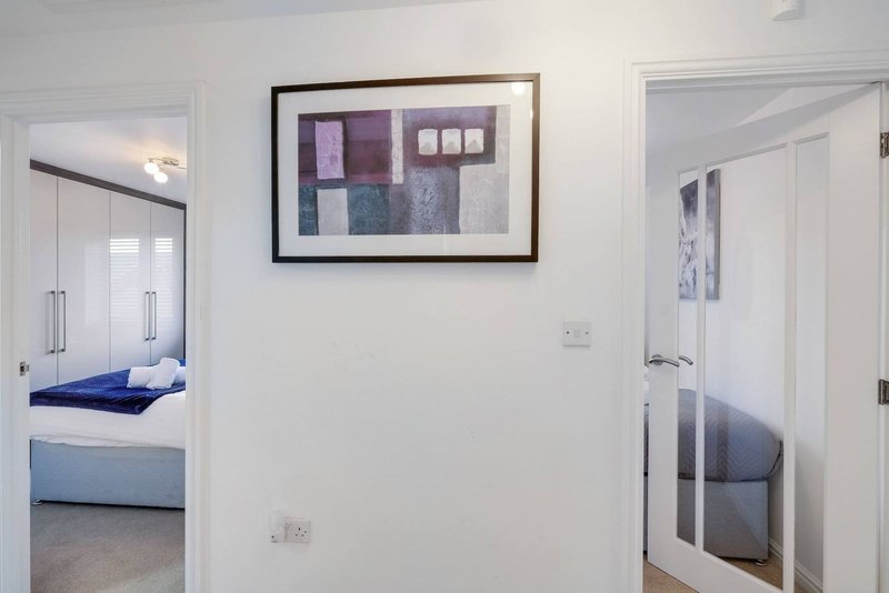 White hallway with framed abstract artwork, doors leading to bedroom and bathroom