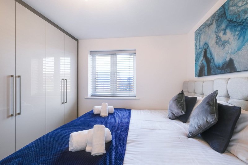 Modern bedroom with double bed, white headboard, blue throw, black cushions and built-in wardrobes