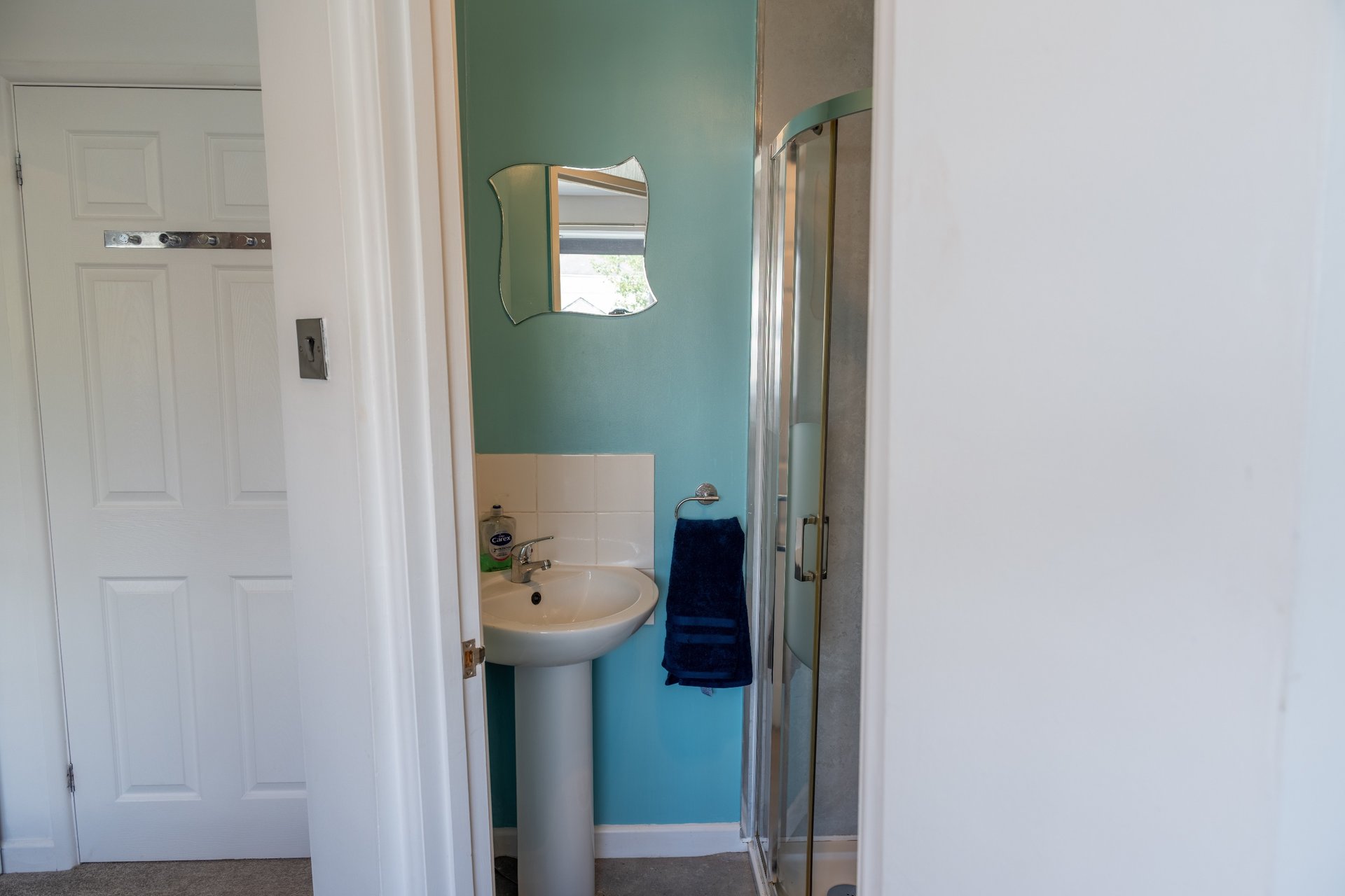 Small bathroom with pedestal sink, mirror, shower enclosure and teal wall