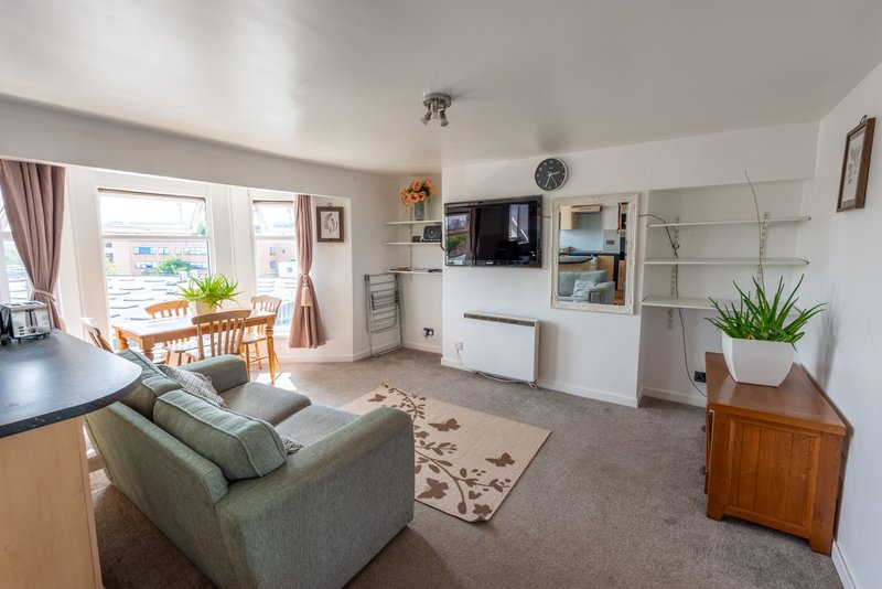 Open-plan living room with sofa, dining table, TV wall, storage shelving and garden views