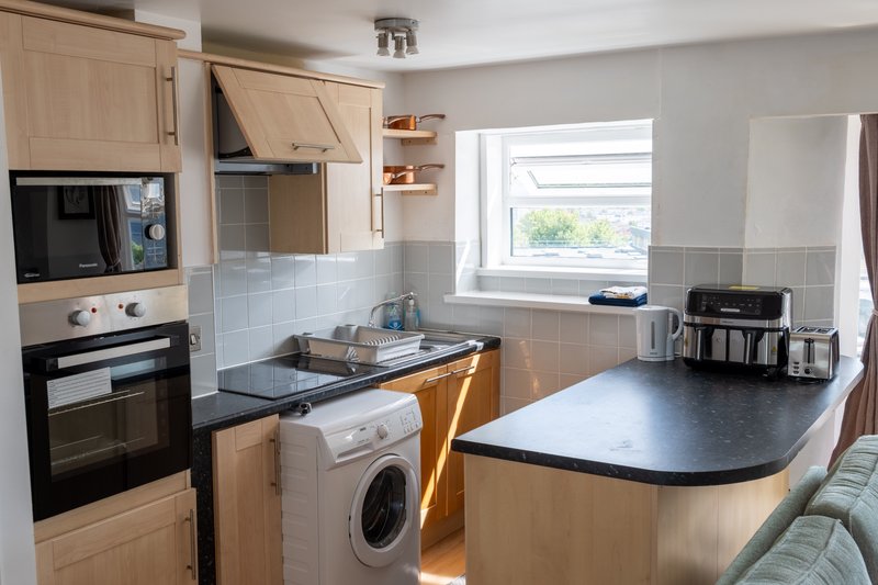 Modern kitchen with light wood cabinets, black countertops, integrated appliances and window