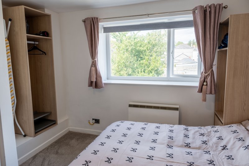 Bedroom with double bed, wooden wardrobes, window with curtains and garden view