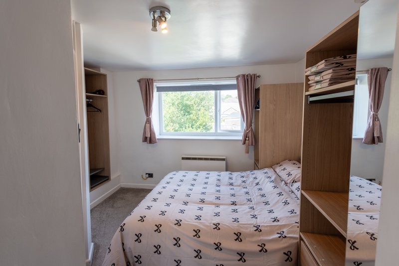 Bright bedroom with double bed, wooden wardrobes, window with curtains and carpet flooring