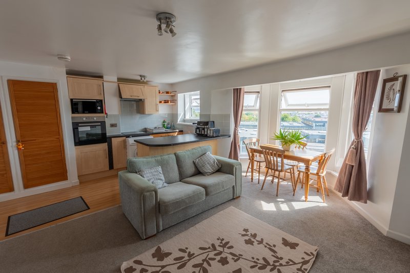 Open-plan living space with kitchen, gray sofa, dining table and patio doors with views