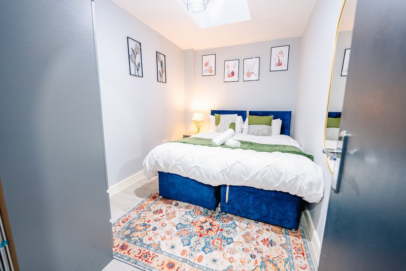 Compact bedroom with blue upholstered bed, white bedding, patterned rug and wall art