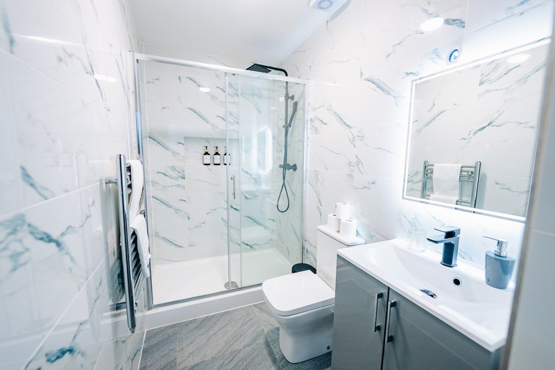 Modern bathroom with marble-effect tiles, glass shower enclosure, white vanity and mirror