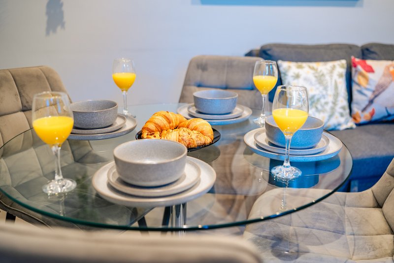 Dining table set with plates, glasses of orange juice, and croissants, blue cushioned seating visible