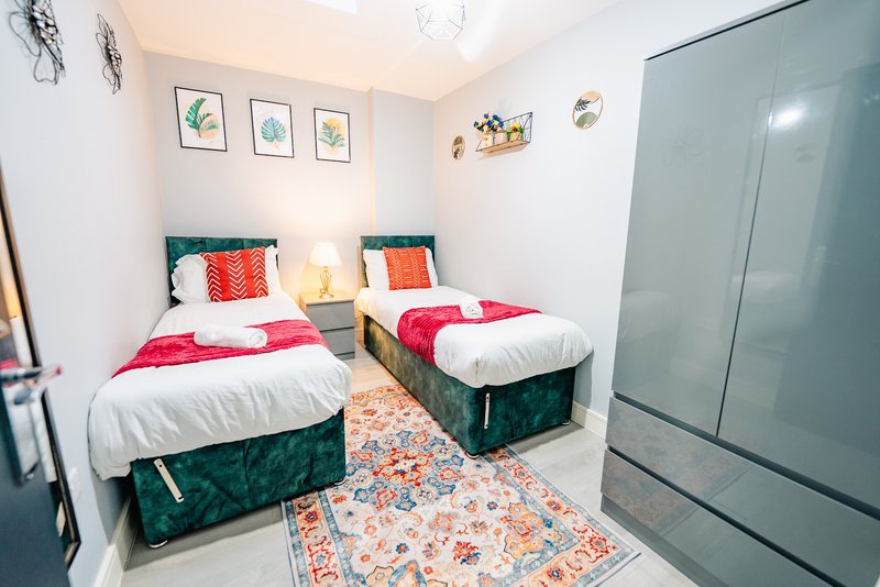 Bright bedroom with two single beds, teal upholstered frames, colorful pillows and white bedding