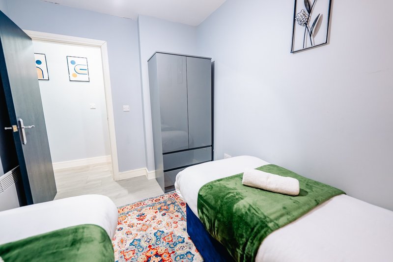 Twin bedroom with white walls, green bedding, wooden floor and wardrobe